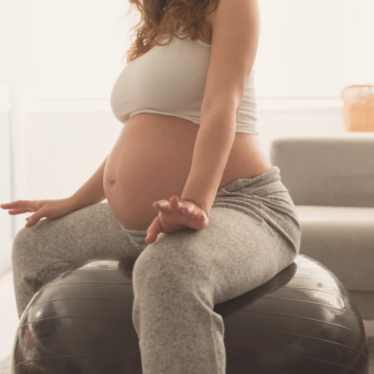 Kobieta w ciąży siedzi na piłce gimnastycznej i ćwiczy mięśnie dna miednicy